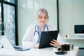 Female doctor reviewing digital records on tablet and writing notes in clinic. Modern healthcare, telehealth, and professional data analysis. in hospital.
