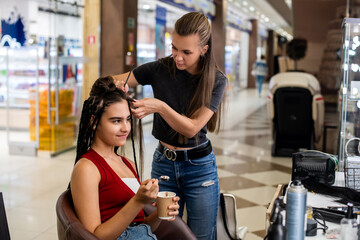 girl gets African braids from a hairstylist while eating ice cream.