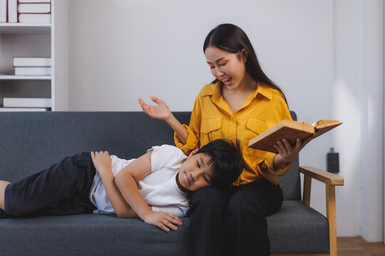 Mother reading a story to her bored son sitting on sofa