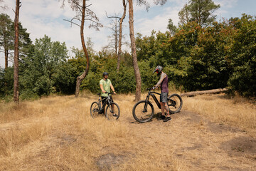 Two individuals with bicycles in a forest taking a break under sunny skies.