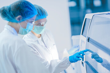Two researchers in a GMP compliant cleanroom operate manufacturing equipment. They are following a Standard Operating Procedure for a Quality Assurance check on a product batch.