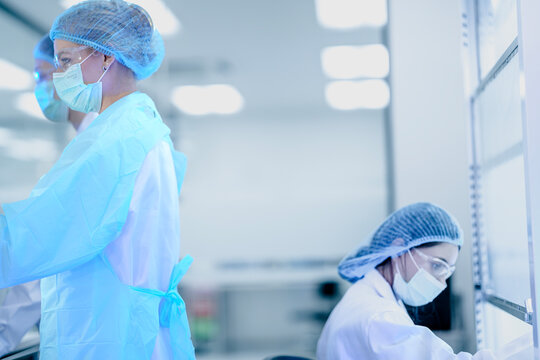 A female scientist in full protective gear works inside a special clean cabinet in a modern lab. She is focused on a careful and important medical experiment to find a cure.