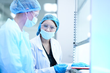 Two researchers in a GMP compliant cleanroom discuss experimental data. They are collaborating to troubleshoot a procedure in a pharmaceutical or biotechnology R and D facility.