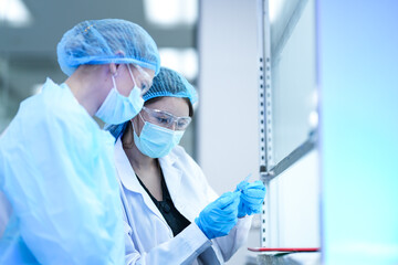Two researchers in a GMP compliant cleanroom discuss experimental data. They are collaborating to troubleshoot a procedure in a pharmaceutical or biotechnology R and D facility.