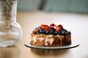 Delicious cake topped with fresh berries on a wooden table beside a glass vase