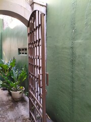 Open wrought iron gate leading to an outdoor space with lush greenery and green walls.
