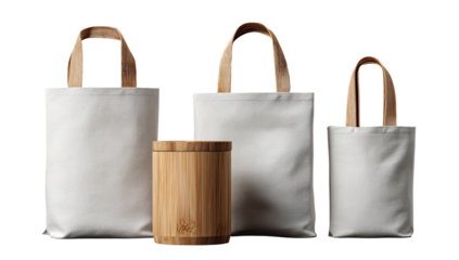 Three white canvas tote bags of varying sizes, alongside a cylindrical wooden container