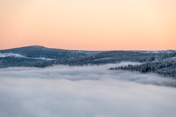 Winter inversion sunset with snow covered hills and forests rising above a sea of clouds, captured...