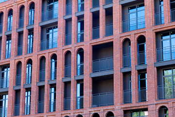 A brick building with arched windows and balconies, designed in a contemporary style. Red brick, metal railings, large windows, and a strict geometric design.