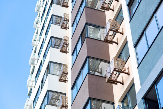 A modern multi-story building with balconies adorned with decorative latticework. The facade is finished in light tones with brown accents. - Powered by Adobe