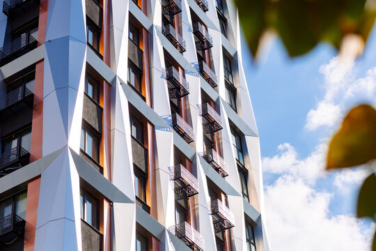 The façade of a modern building features geometric accents, cantilevered balconies, and large windows. White panels contrast with orange elements.
