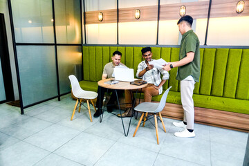 Three Male Colleagues Collaborate and Review Documents and Data on Laptop in Modern Office Setting