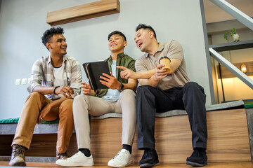 Three Young Men Sitting and Talking While Looking at Tablet in Office