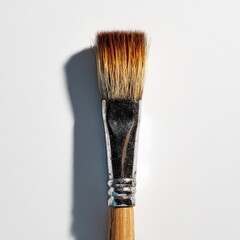 Flat paintbrush with worn, natural bristles, wooden handle, metallic ferrule, cast shadow on white background