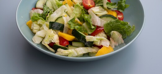 Bowl of mixed salad with lettuce leaves, cucumbers, cherry tomatoes, and mango. Healthy vegetarian food rich in vitamins, fresh organic meal for diet and wellness, isolated on gray background.