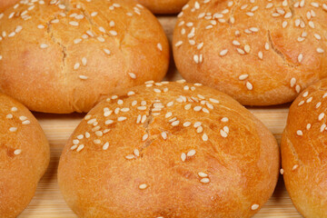 A close-up shot capturing a cluster of fresh, homemade sesame seed buns on a rustic wooden board