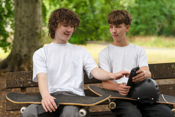 Fototapeta premium Friends enjoying a sunny day at the park while discussing skateboarding tricks and checking their phones