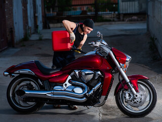 Naklejka na ściany i meble Caucasian woman refueling motorcycle from canister. 