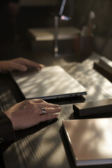 Close-up of man’s hands closing laptop at office desk under warm sunlight, symbolizing end of workday or business pause.