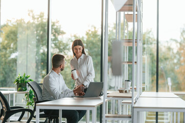 Working by using laptop. Man and woman are in the modern office together