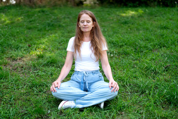 Fototapeta premium Woman practicing meditation on a green lawn in a peaceful outdoor setting during the day