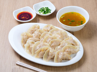 Chinese dumplings served with a small bowl of condiments, including scallions and chili sauce