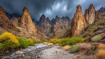 Dramatic desert canyon scene with towering rock formations, a dry creek bed, and vibrant yellow desert shrubs under a stormy sky