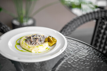 Elegant plated dish with mashed potatoes, creamy mushrooms, grilled zucchini, and herb oil garnish, served outdoors on a white plate with natural light and rustic background