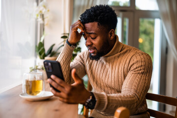 Young black man sitting in bar. He is freelancer on job pause, tired and exhausted.