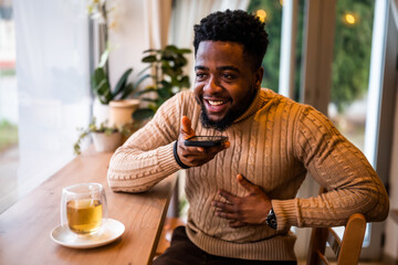 A young black man sits at the bar, casually dressed. He is using smartphone and recording voice...