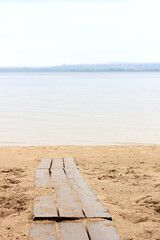 A path made of wooden beams on a sandy beach leading to a river in cloudy weather
