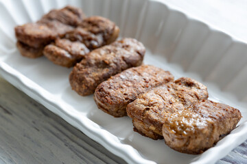 Close-Up of Romanian Mici Sausages Served with Flatbread and Tomatoes on a White Plate
