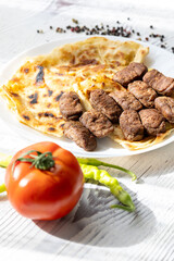 Close-Up of Romanian Mici Sausages Served with Flatbread and Tomatoes on a White Plate
