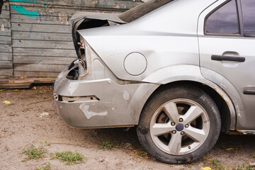 Fototapeta premium Damaged silver sedan parked near a rundown building in the afternoon