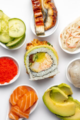 Sushi roll on a white background, and around it are white spoons with ingredients. Salmon, shrimp, tuna