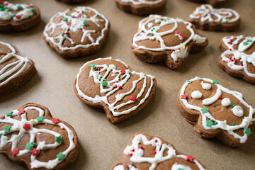 Homemade Christmas gingerbread cookies decorated with white icing and colorful sprinkles on brown baking paper, close-up