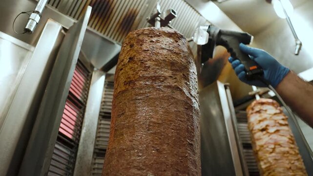 Chef slices meat from a rotating doner kebab indoors. Ideal for restaurant, culinary preparation, and Middle Eastern cuisine themes, highlighting food craftsmanship and meal presentation.