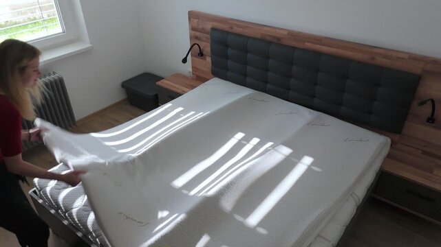 Caucasian blonde woman installing mattress topper on a new bed, indoor, medium shot