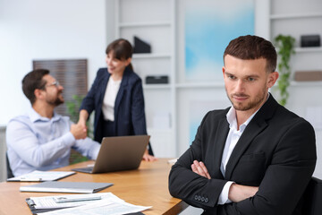 Fototapeta premium Man feeling jealous of his successful colleague receiving congratulations in office, selective focus
