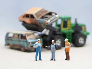 Mini toy of action figure at table with blurred background. Business photography concept design. Minifigure of mechanic crew with damage car and bulldozer at junk yard.