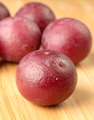 Close-up of several round, deep-red fruits on a light-colored wooden surface