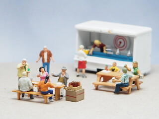 Mini toy of action figure at table with blurred background. Business photography concept design. Minifigure people character eating food at outdoor cafe with foodtruck. Group of people at foodcourt.
