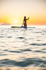 Calm young woman paddleboarding in ocean at sunset