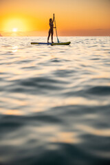 Serene young woman paddleboarding at ocean during sunrise
