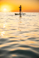 Young woman paddleboarding in ocean at sunset, serene mood