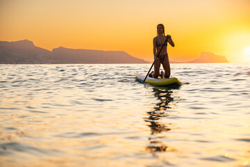 Young woman paddleboarding in calm ocean at sunset