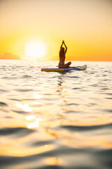 Calm woman meditating on paddleboard at sunrise over ocean