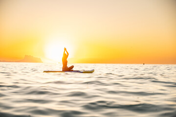 Young woman practicing yoga on paddleboard at sunrise