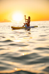Serene woman paddleboarding at sunset on the ocean