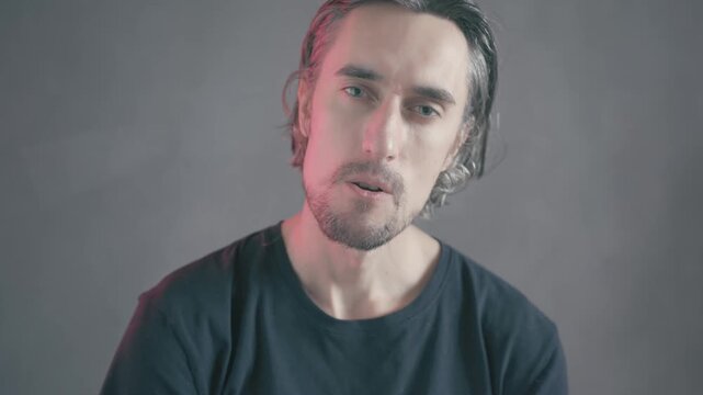 Comically Saluting Young Attractive Male Character with Bearded Face, Striking a Serious Pose Against Muted Grey Background and Dramatic Pink Lighting